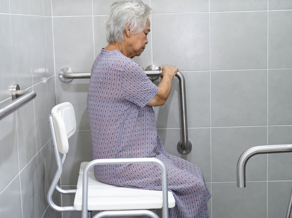 Picture of a woman sitting on a plastic medical bench holding onto grab bars.
